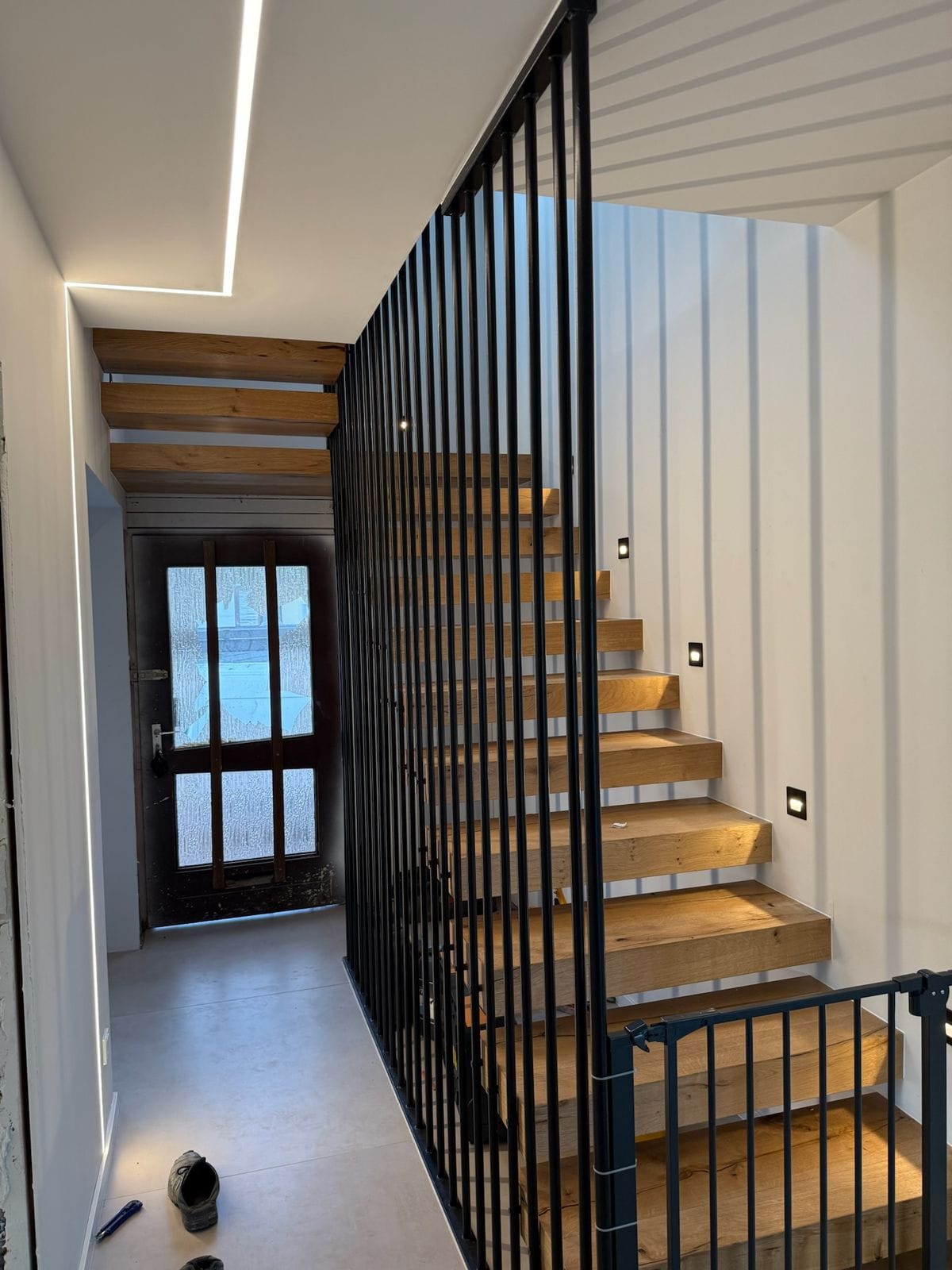 Großzügiger, fugenlos wirkender Bodenbelag im Eingangsbereich mit freitragender Treppe