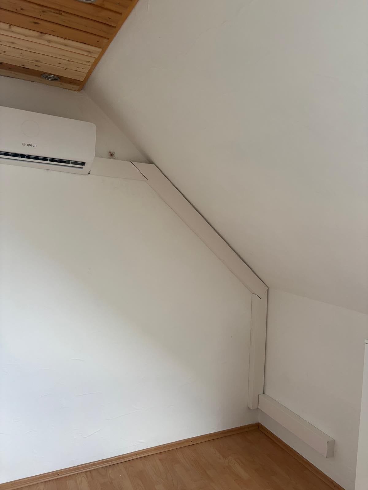 Weißes Split-Innengerät unter einer Dachschräge, die Leitung läuft im schmalen Kanal an der Schräge entlang bis zur Fußleiste